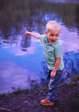 Toddler in light blue shirt and jeans plays excitedly by a reflective pond.