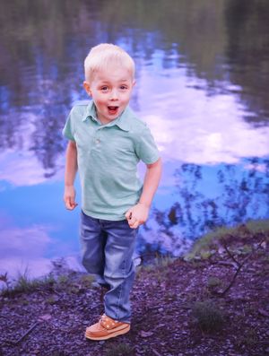 Young child in casual wear laughs while playing near water's edge.