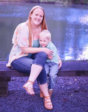 Mother and child share tender moment sitting by lake on rocky shore.