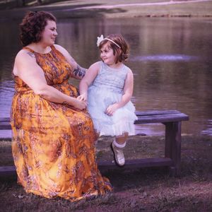 Family photoshoot by a lake with orange floral dress and white outfit creating warm sunset moments.