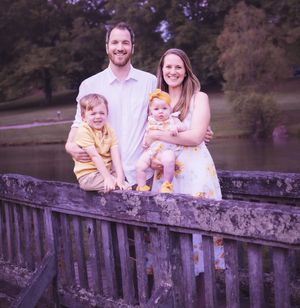 Family of four poses together on wooden bridge over tranquil water.