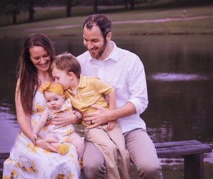 Happy family wearing coordinated outfits poses by lake during sunset.