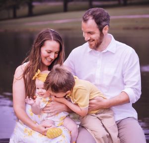 Family shares joyful embrace during outdoor photo session by water.