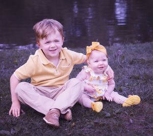 Children in yellow outfits play together on grassy lakeside during family photoshoot.