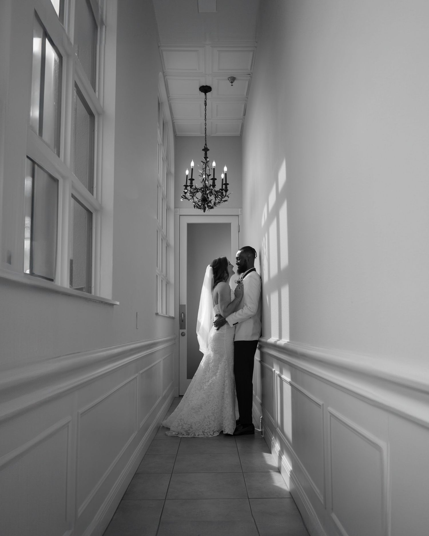 A romantic black and white hallway scene with an ornate chandelier and elegant wainscoting.