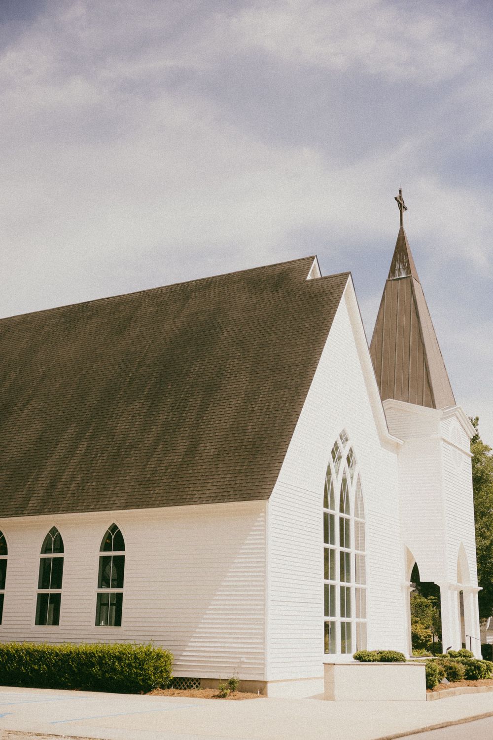 Traditional white church with gothic windows and tall steeple against cloudy sky.