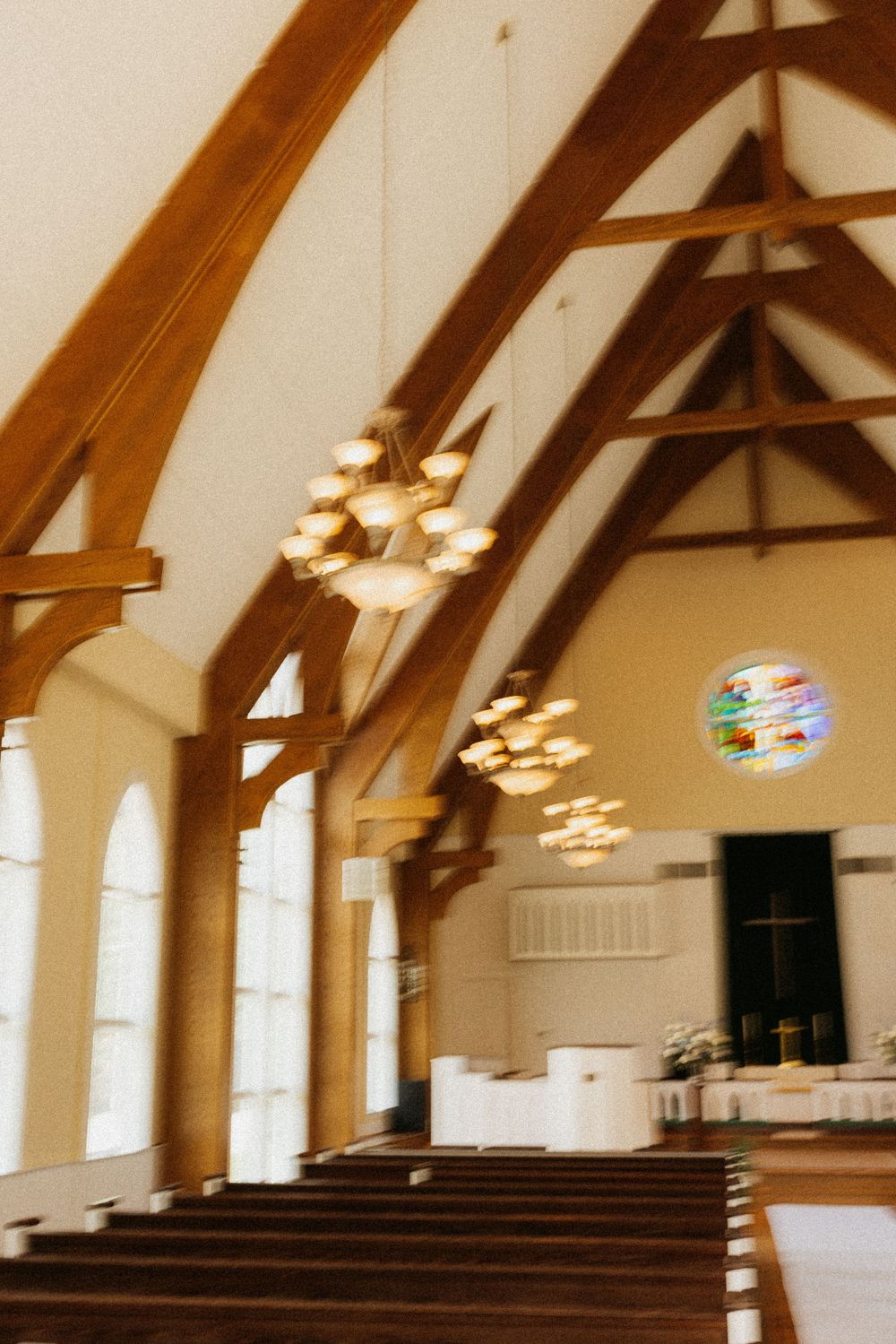 Warm-toned interior photograph of church featuring wooden beam architecture and hanging chandeliers.