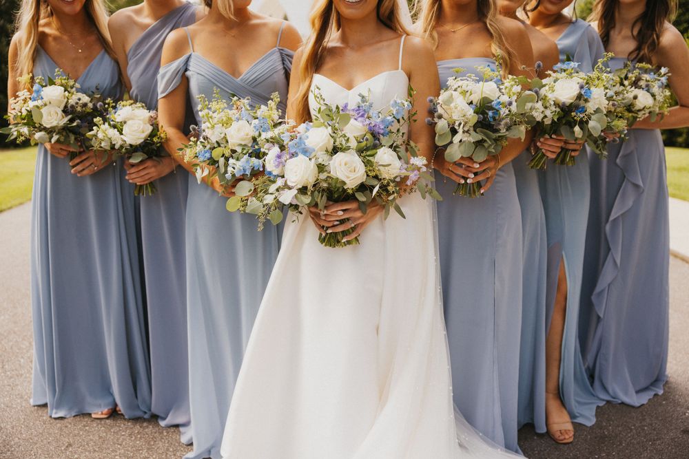 A row of bridesmaids in light blue dresses holding white and blue flower bouquets.