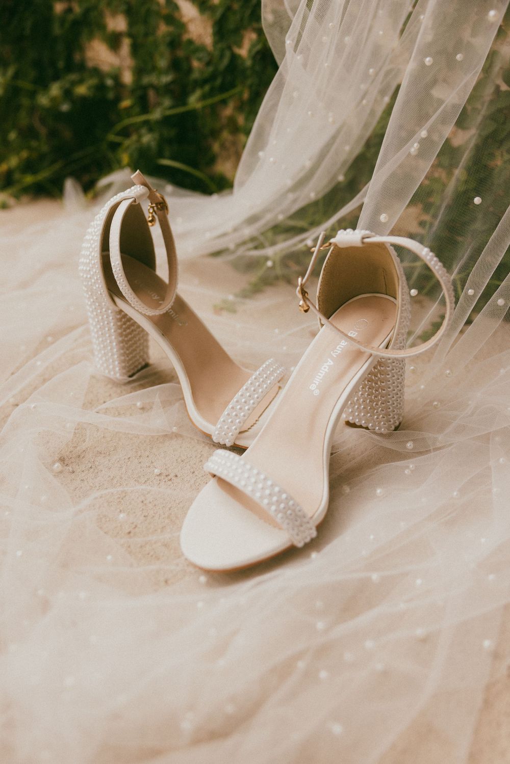 White wedding heels with pearl detailing resting on tulle veil.