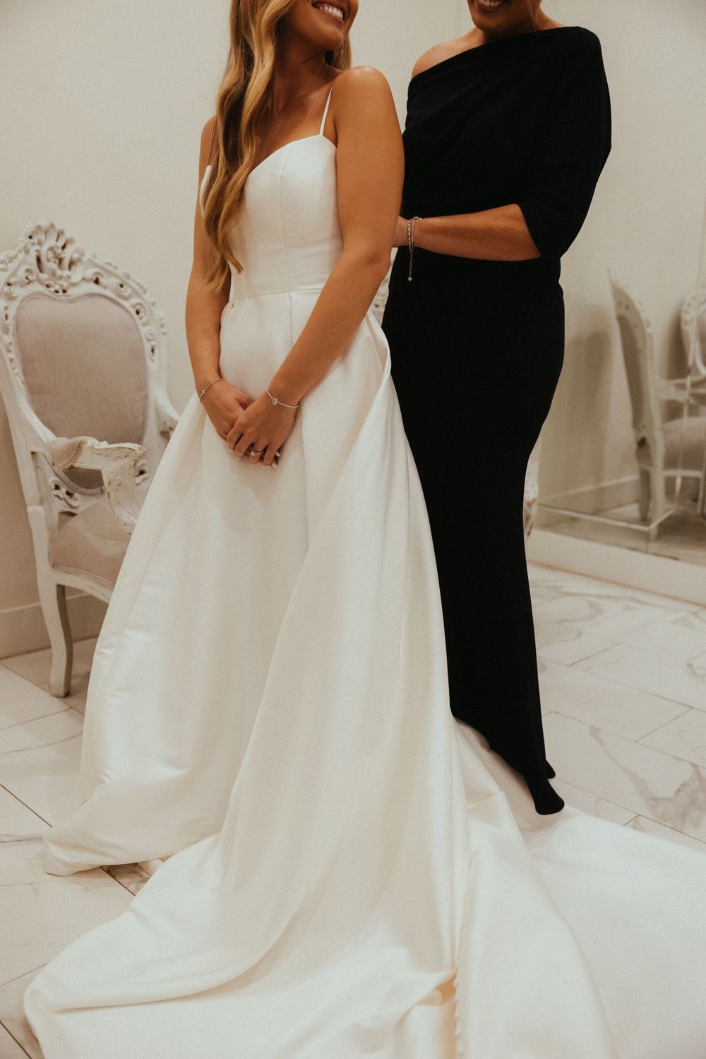 Bride in classic white wedding gown standing next to person in black outfit.