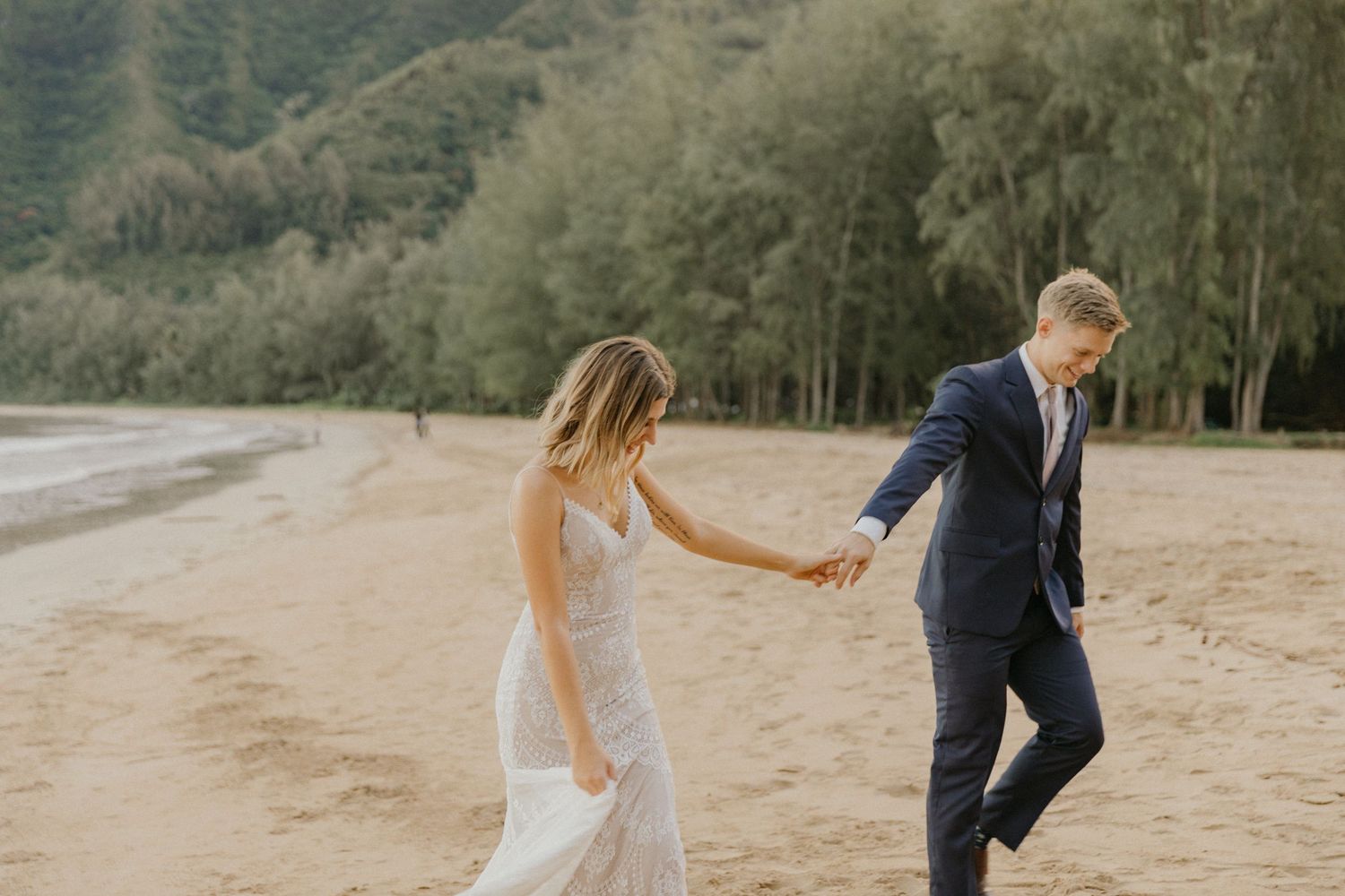 Orlando Luxury Wedding Photographer a couple walks hand in hand along a peaceful beach with a forest backdrop during their wedding day.
