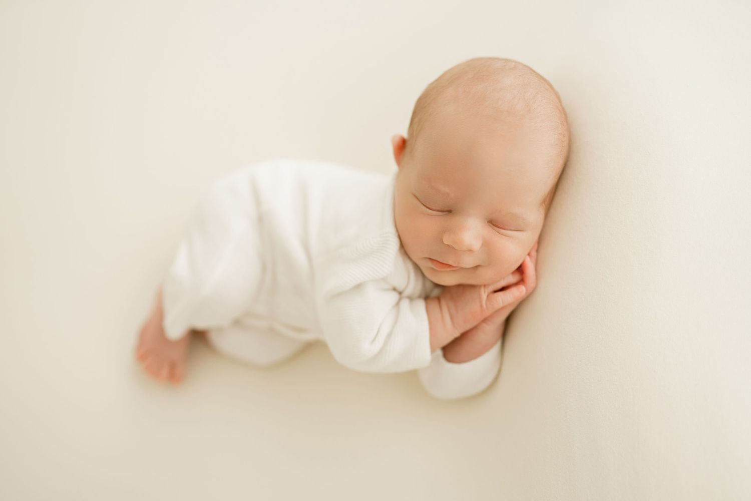 Peaceful sleeping newborn in white outfit against cream background.
