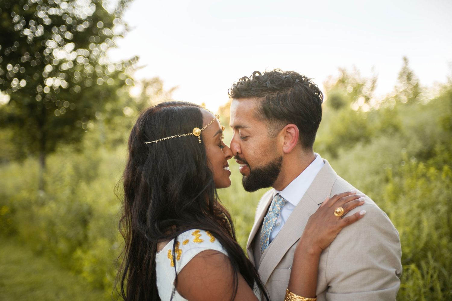 Golden hour wedding photo bride and groom touching noses and smiling. Romantic, authentic, classic, sweet. Greenery is lit up by sunset.