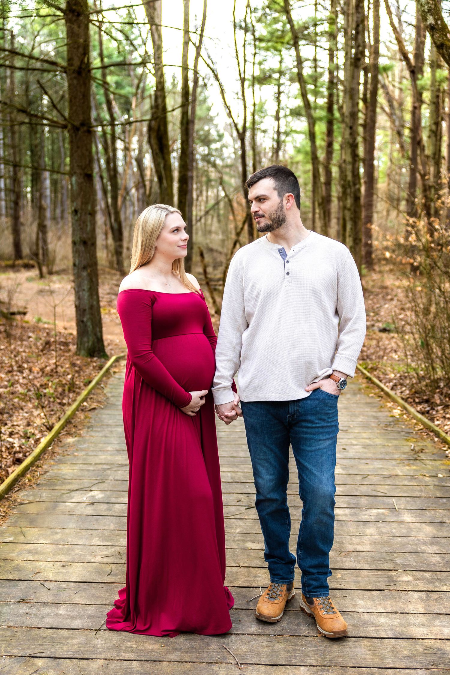 A couple walks together on a wooden boardwalk path through a serene forest setting wearing burgundy and white outfits.