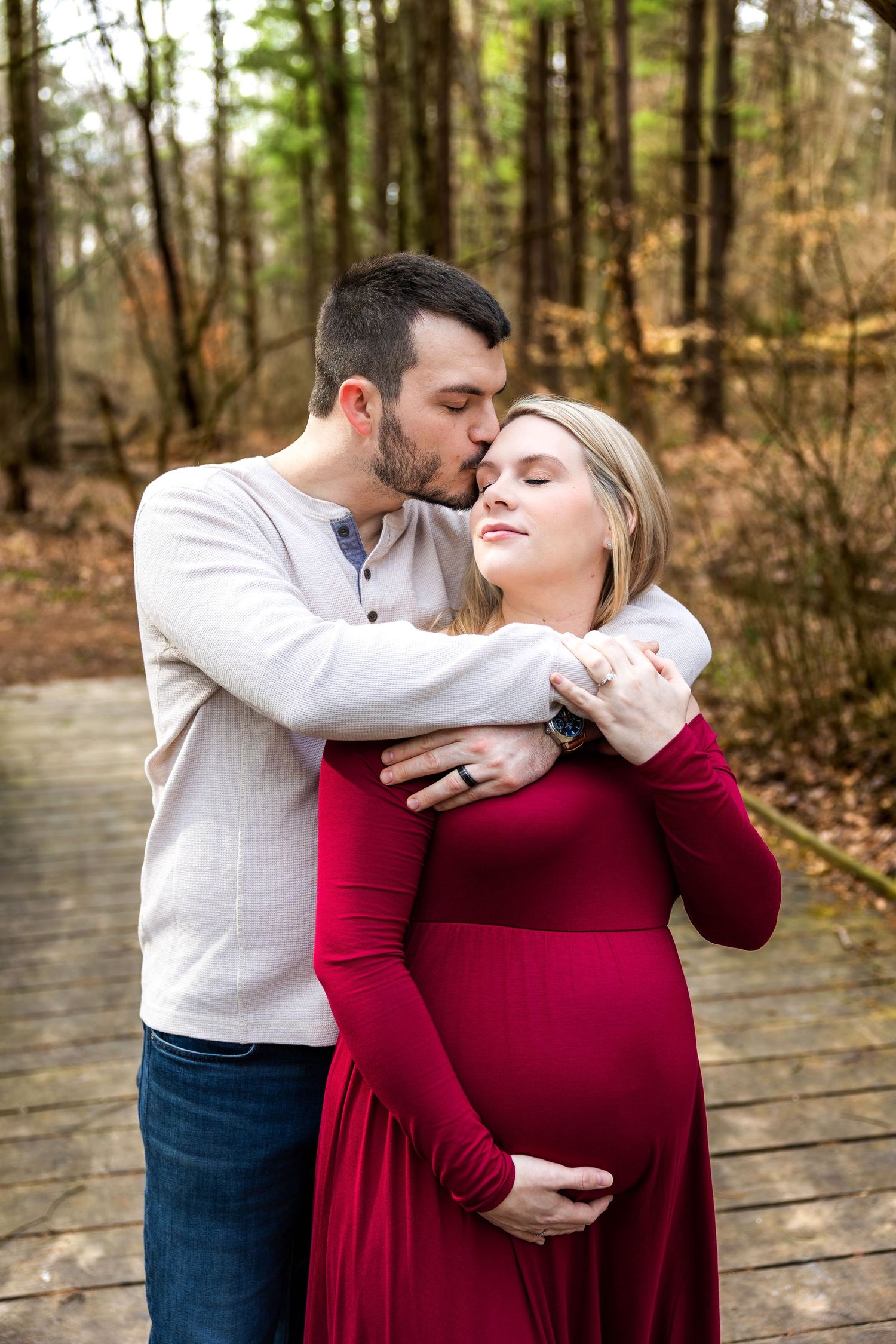 A couple shares an intimate moment on a wooden boardwalk surrounded by autumn trees in the forest.
