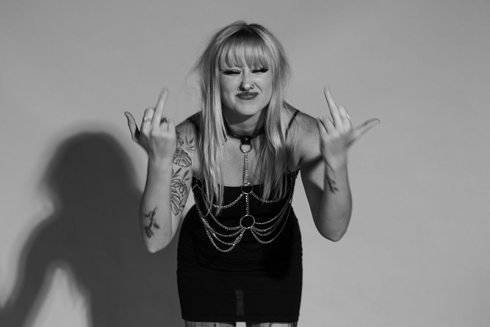 Candice (Bandicex) is photographed in black and white flipping off the camera. The background is white and her hair is mussed.