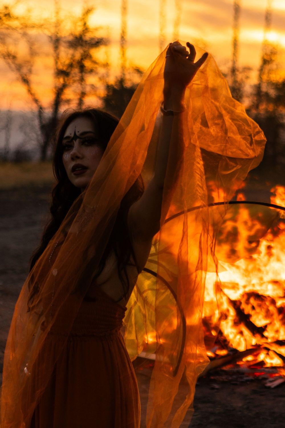 Young model dressed in orange as a fairy in front of a fire