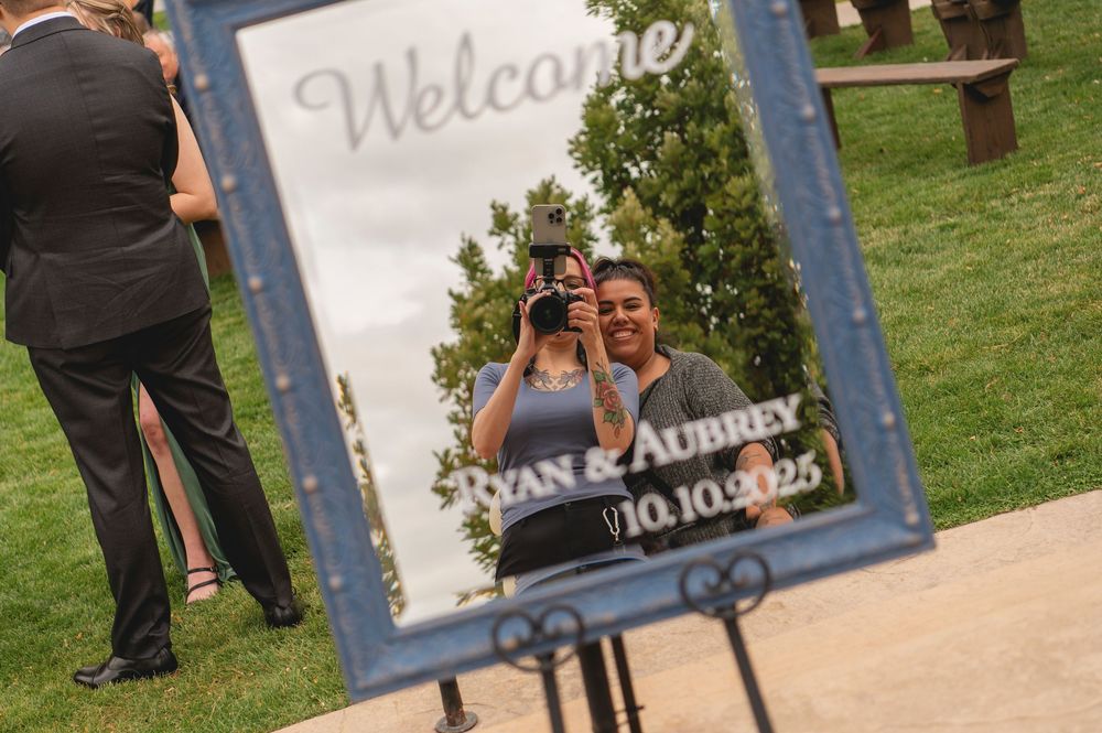 Photographer reflects in a decorative welcome mirror sign for Ryan & Aubrey wedding on 10.10.25 outdoors.