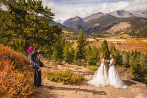 Wedding photographer capturing LGBTQ+ couple's portraits in scenic Rocky mountain National Park setting with fall colors.