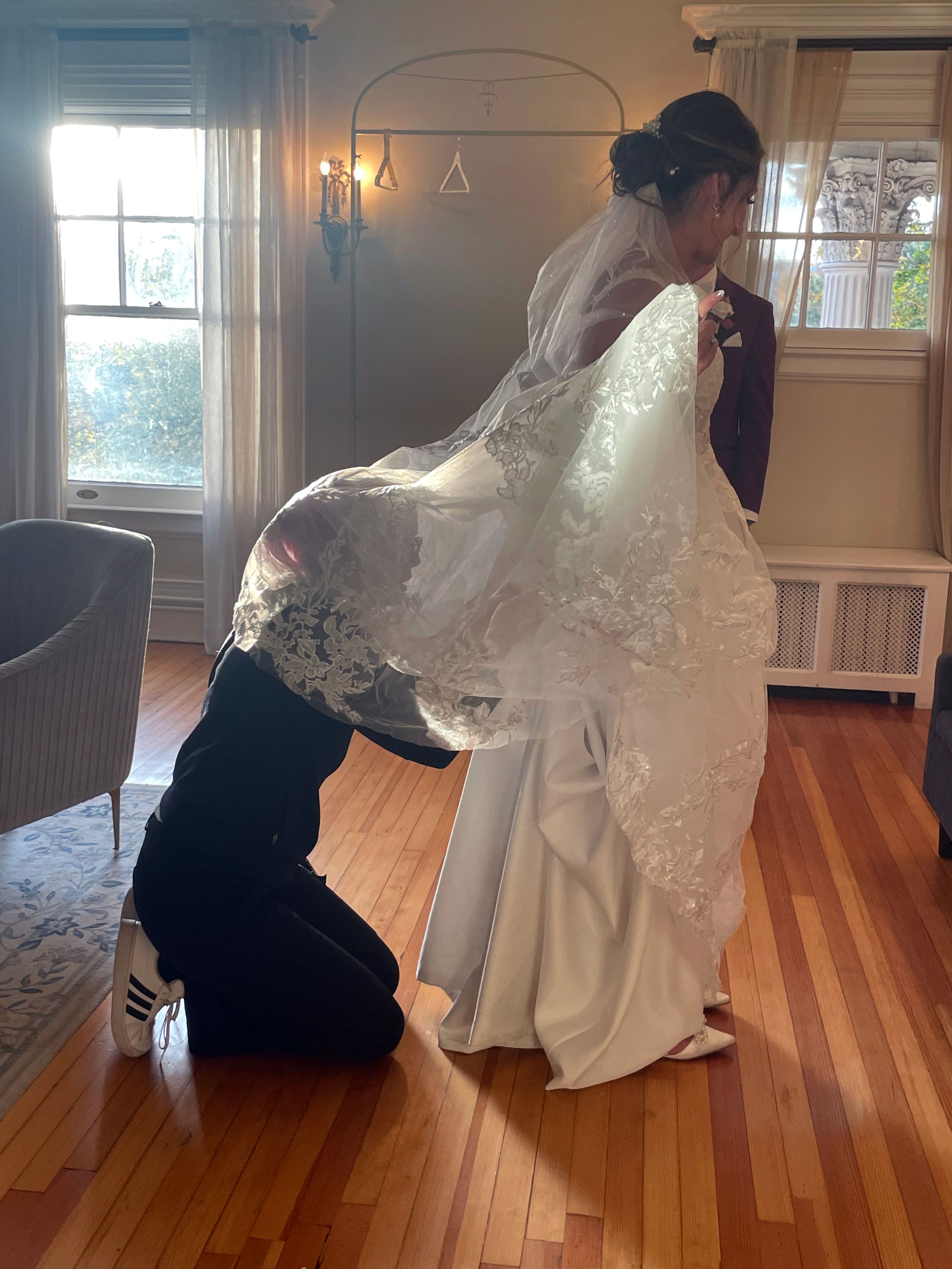 Wedding dress being adjusted in sunlit room with hardwood floors.