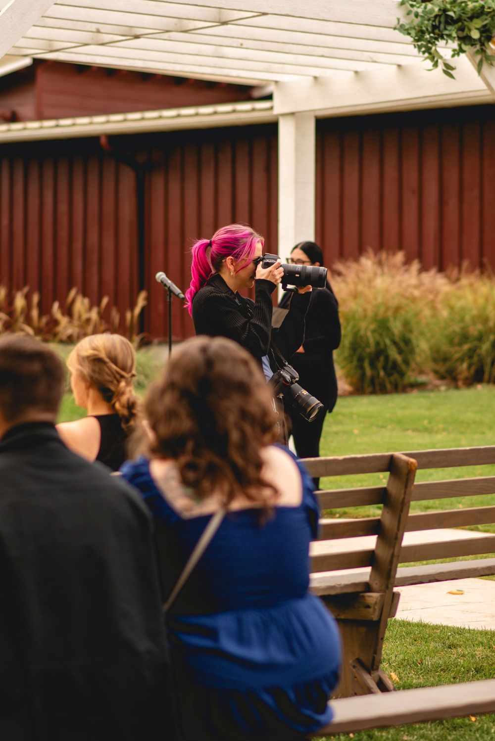 Photographers with cameras line up on wooden benches to capture shots at an outdoor event.