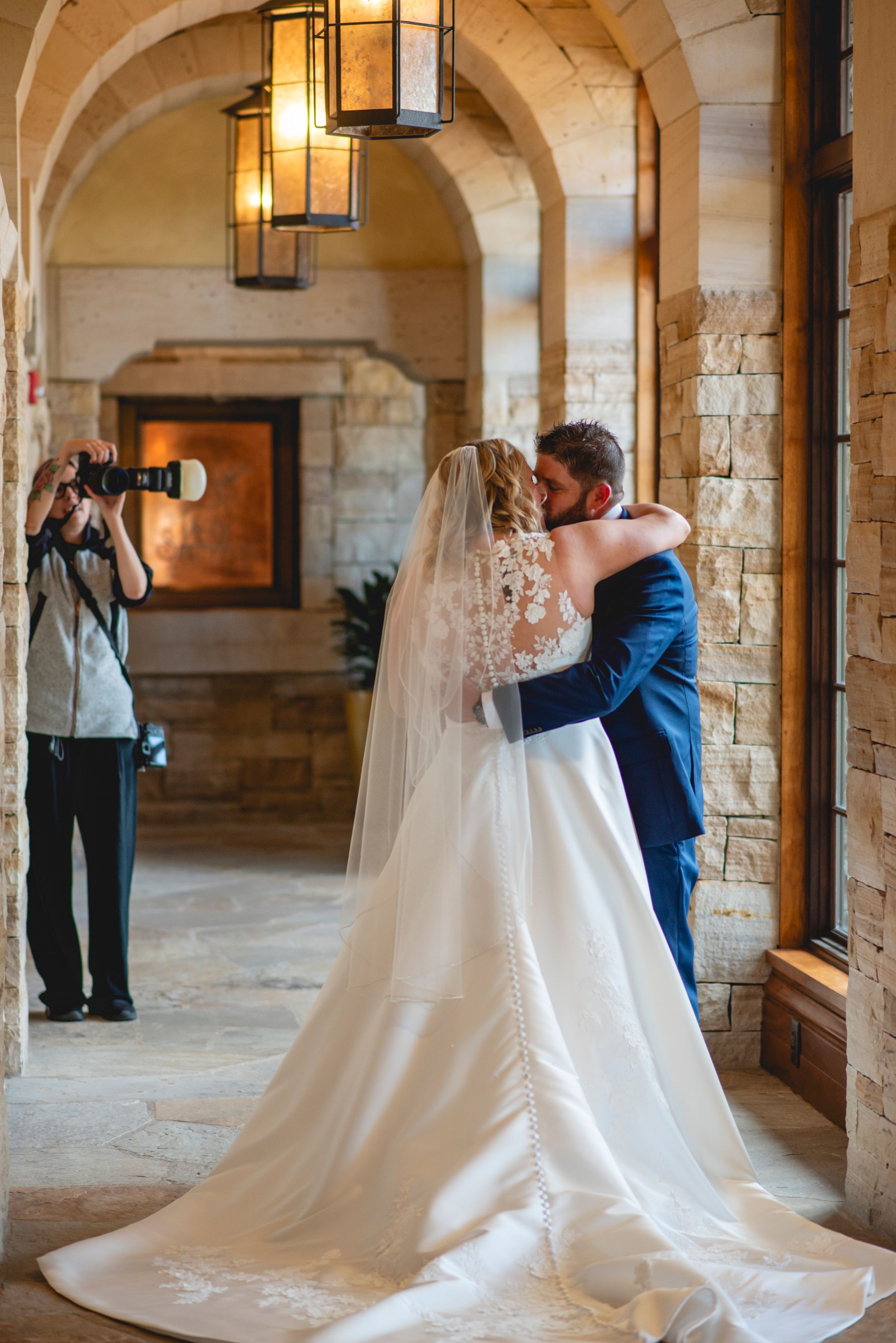 Wedding photographer captures couple embracing in stone archway with elegant gown and veil trailing behind at The sanctuary golf course.