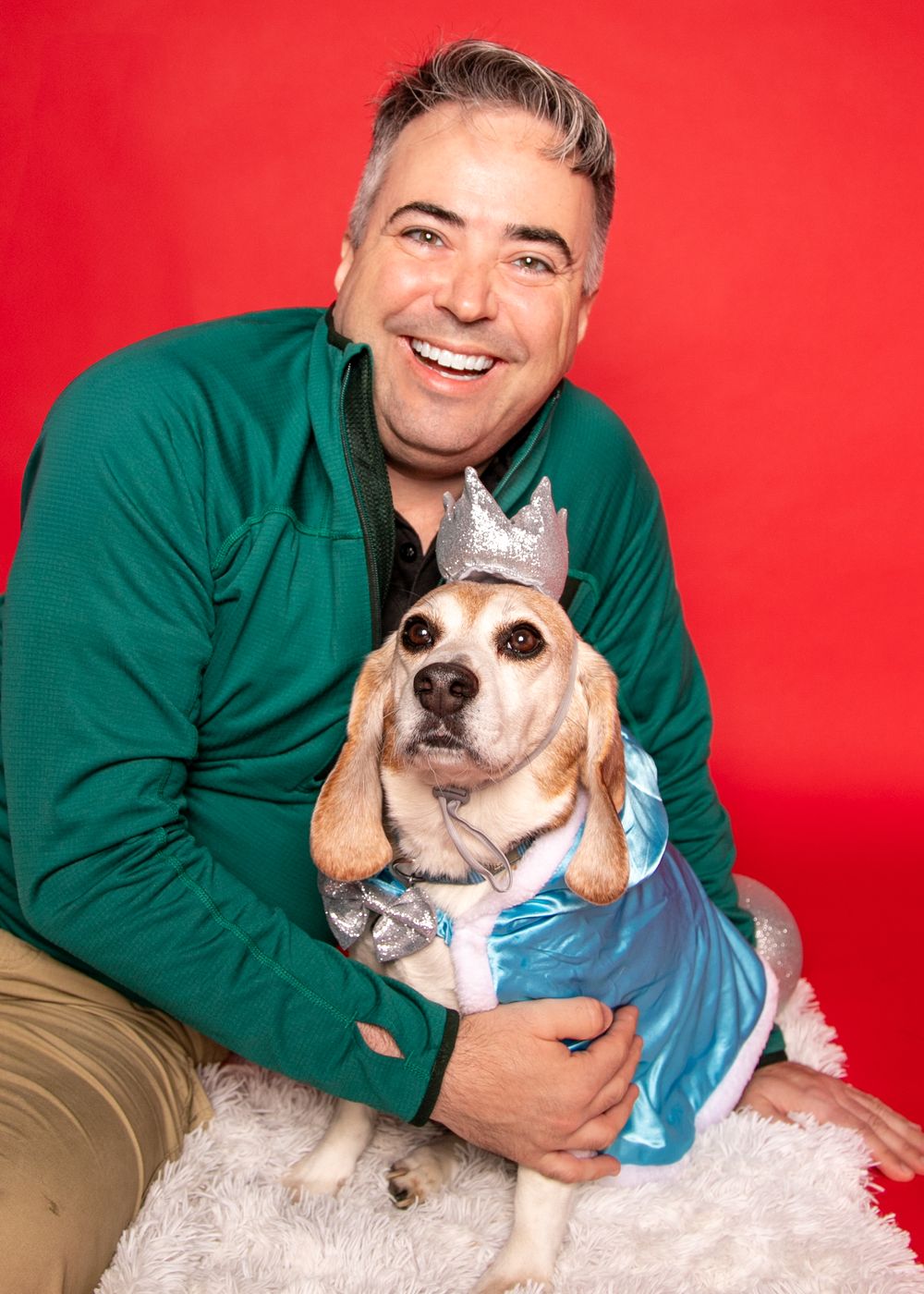 Dog in light blue outfit cuddling on red background.