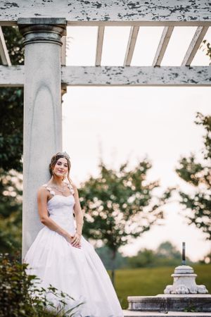 Bride in elegant white gown poses under pergola during sunset.