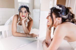 Reflection of a bride in an elegant white dress looking dreamily into a mirror.