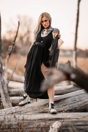 Alternative fashion portrait on fallen logs featuring a flowing black dress and combat boots.