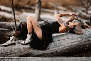 Dramatic portrait on driftwood wearing a black dress and sneakers.