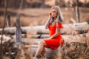 Portrait in bright red dress sitting on fallen logs during sunset.