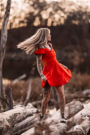 Dynamic fashion shot in flowing red dress against rustic outdoor setting.