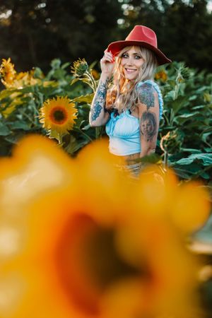 Portrait among vibrant sunflowers with a red hat and blue top during golden hour photography.
