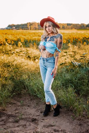 A stylish photoshoot in a sunflower field featuring denim jeans, crop top, red hat and boots at sunset.