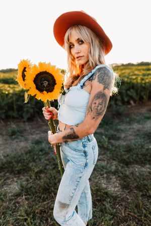 Casual summer portrait with sunflowers and denim overalls in golden light.