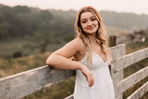 A white sundress outfit is showcased against a rustic wooden fence in golden hour lighting.