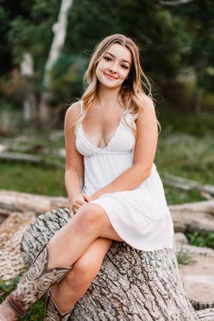 White summer dress styled with boots for outdoor portrait on rustic log setting.