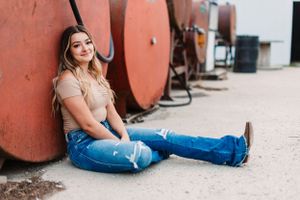 Casual style featuring distressed jeans and neutral top while sitting against industrial backdrop.