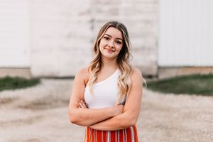 Casual summer outfit with white tank top and striped pants against neutral backdrop.