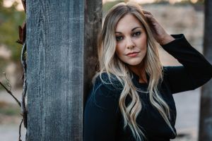 Moody portrait against wooden post featuring dark sweater in natural lighting.