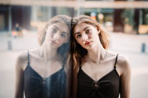 Artistic double exposure portrait through glass with black dress and subtle reflection.