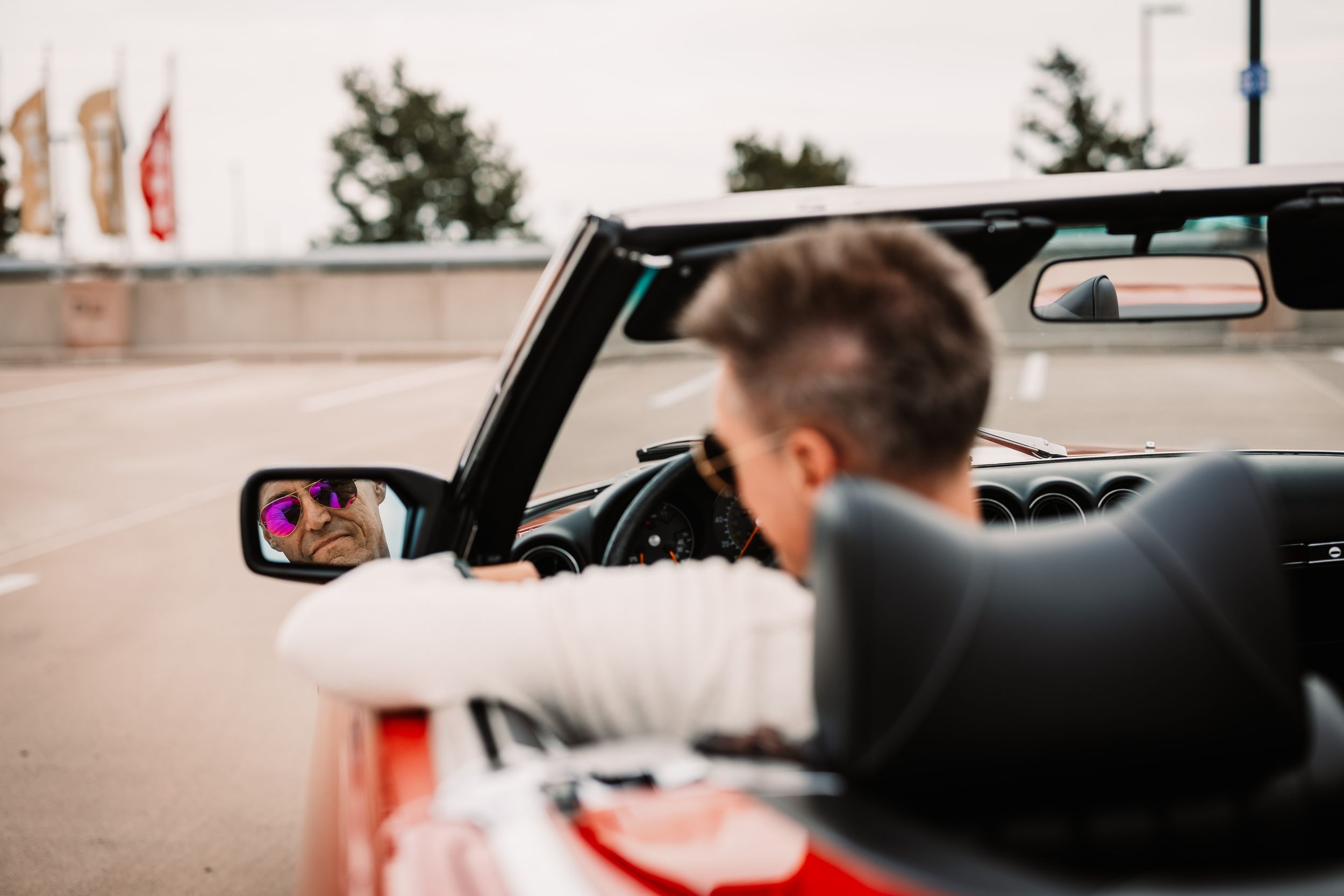 Person driving a classic convertible car viewed through side mirror.