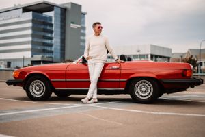 Classic red Mercedes convertible with person in white outfit standing beside it.