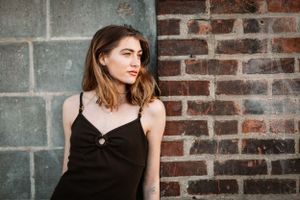 Fashion portrait against rustic brick wall featuring black slip dress and casual urban style.