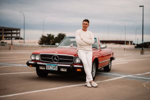 Vintage red Mercedes-Benz SL convertible parked in empty lot with contemporary buildings.