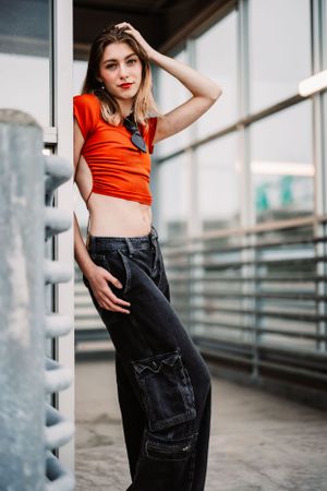 Urban fashion portrait with orange crop top and cargo pants against modern architecture.