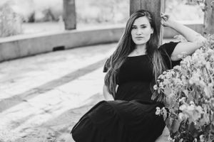 Black and white portrait of woman in flowing dress posed against stone wall.