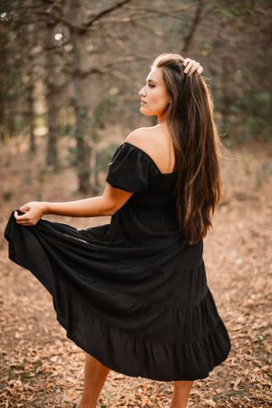 Woman in black dress twirling in autumn forest setting.