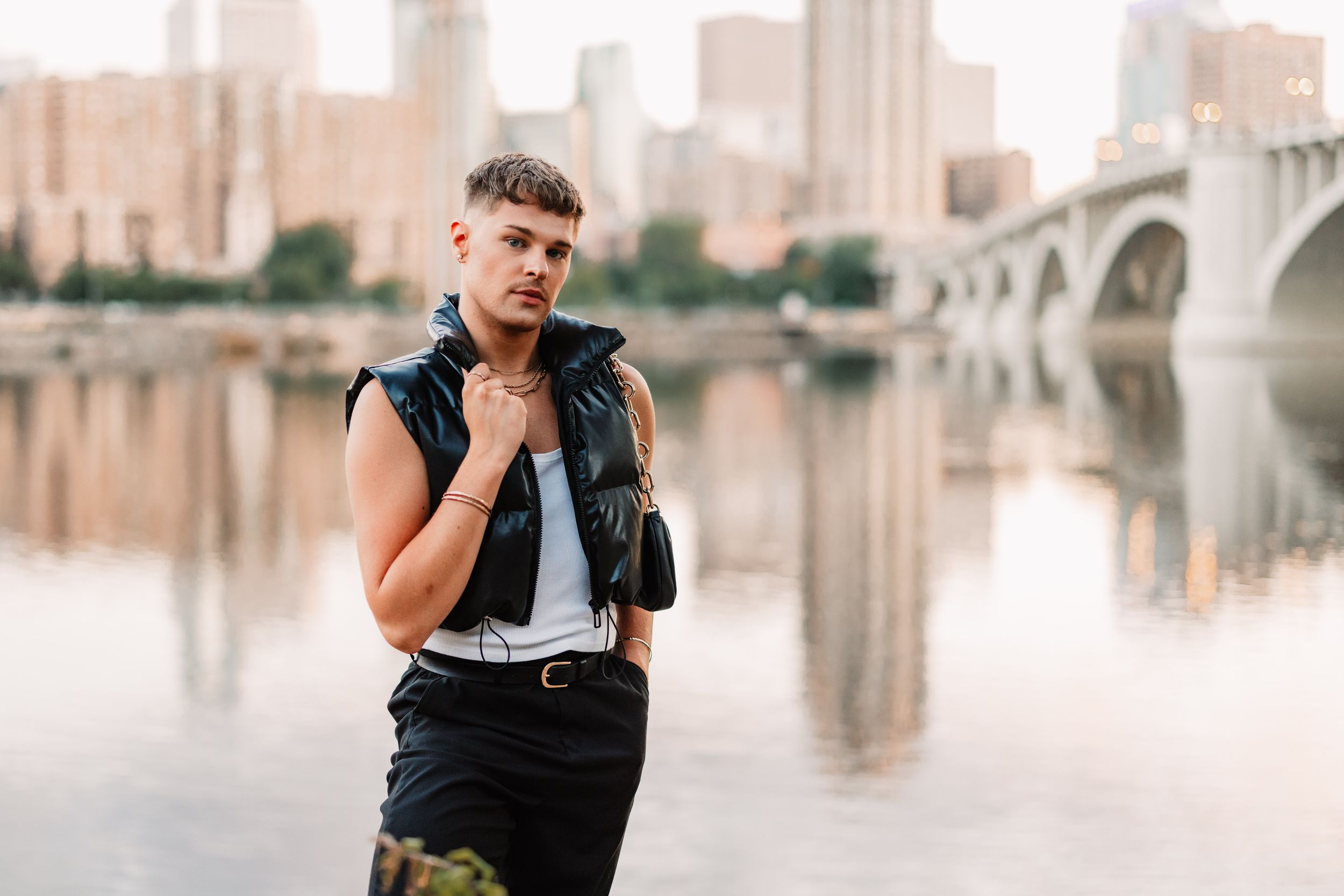 Person in black attire poses confidently against urban backdrop in professional fashion photoshoot.